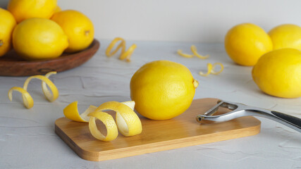 Wooden board, lemons, peeler and fresh rind on white textured table