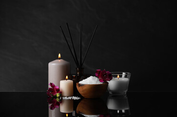 Beautiful spa composition with different care products and burning candles on mirror table against black background