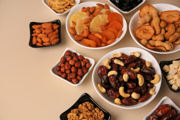 Bowls with dried fruits and nuts on beige background, above view. Space for text