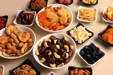 Bowls with dried fruits and nuts on beige background