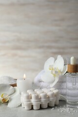 Fototapeta na wymiar Beautiful composition with different spa products, burning candles and flowers on light grey table. Space for text