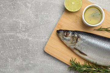 Wooden board with salted herring, lime, oil and rosemary on grey table, top view. Space for text