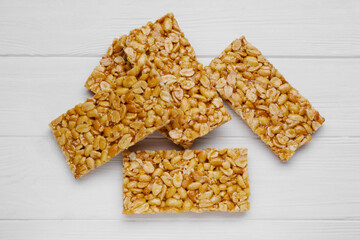 Tasty peanut bars (kozinaki) on white wooden table, flat lay