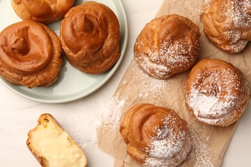 Delicious profiteroles with powdered sugar on white table, flat lay