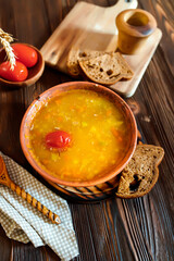 Tomato soup in a clay plate on a wooden vintage farm table near a piece of brown bread.