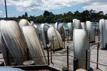  Several rowing boats are stood upright in a storage area on wooden decking.An estuary with other...