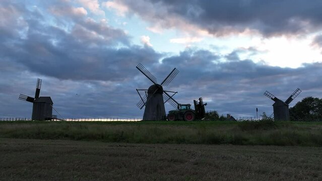 Landscape with windmills and a tractor passing in front of them. Angla village in Saaremaa, Estonia.