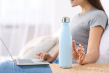 Woman with laptop taking thermo bottle in bedroom, closeup. Space for text