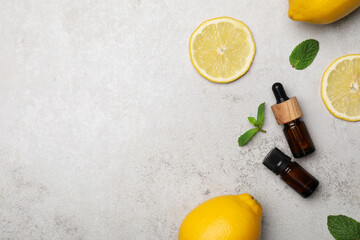 Bottles of citrus essential oil and fresh lemons on light table, flat lay. Space for text