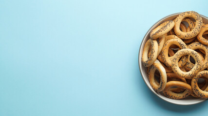 Bowl with delicious ring shaped Sushki (dry bagels) on light blue background, top view. Space for text