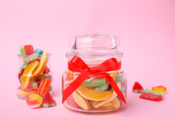Glass jars with tasty colorful jelly candies on pink background