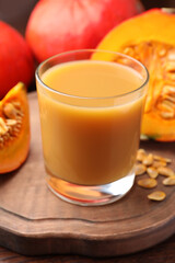 Tasty pumpkin juice in glass, whole and cut pumpkins on wooden table, closeup
