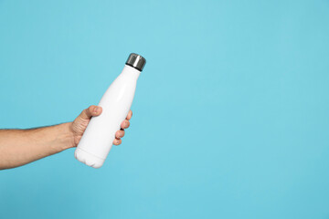Man holding thermo bottle on light blue background, closeup. Space for text