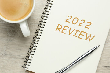 Text 2022 Review written in notebook, pen and cup of coffee on wooden table, top view