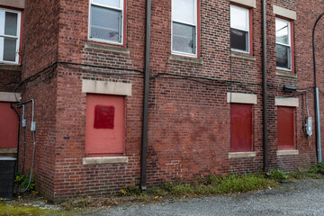 Rear of an urban apartment building, lower windows blocked with red painted boards, horizontal aspect