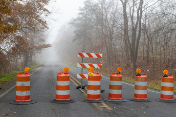 Row of tightly spaced orange traffic barrels barricading a road disappearing into a foggy autumn...