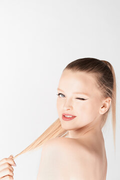 Portrait of attractive blond-haired girl with naked shoulders and high ponytail looking at camera and winking on white background  