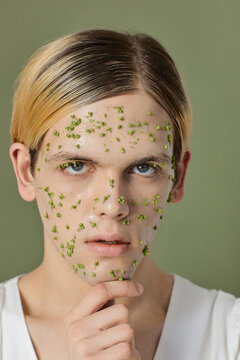 Young man with very small green flowers on his face touching his chin
