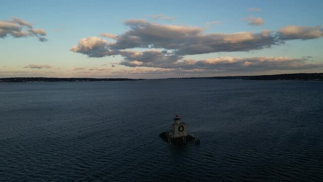 A high angle, aerial view of the Huntington Harbor Lighthouse on Long Island, NY at sunset, with a Christmas wreath. The camera truck left and pan right around the lighthouse with blue sky and clouds.