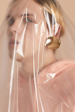 Portrait of feminine male model with golden earring covered with polythene sheet looking at camera