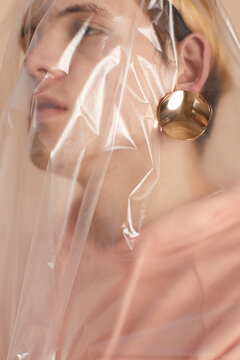 Portrait of handsome feminine male model with golden earring covered with polythene sheet looking away