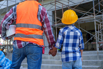 Male contractor holding boy's hand standing looking at building under construction, father taking...