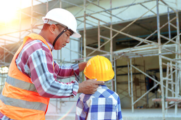Plakat Male contractor holding boy's hand standing looking at building under construction, father taking son to look at his construction site, low view from behind, father and son holding hands.