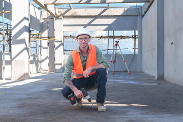 Male engineer wearing safety suit and hard hat holding toolbox and electric drill in construction site for building site survey in civil engineering project.