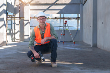 Male engineer wearing safety suit and hard hat holding toolbox and electric drill in construction site for building site survey in civil engineering project.