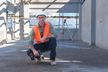 Male engineer wearing safety suit and hard hat holding toolbox and electric drill in construction site for building site survey in civil engineering project.