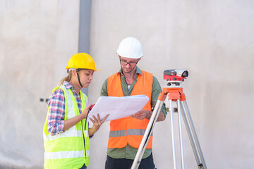 Construction Worker Using Theodolite Surveying Optical Instrument for Measuring Angles in Horizontal and Vertical Planes on Construction Site. Engineer and Architect Using blueprint Next to Surveyor.