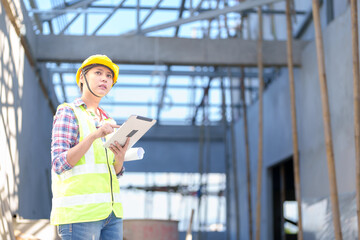 Asia Female civil engineer with inspecting construction plans at building site of high-riser building site survey in civil engineering project.