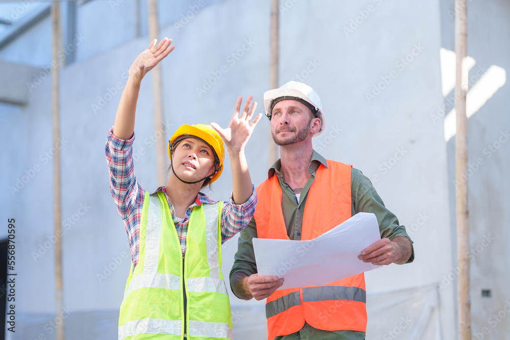 Wall mural Two professionals inspect construction site of commercial building, industrial building, real estate project  civil engineer, investor using laplet in background crane, skyscraper, concrete formwork