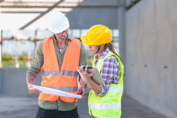 Two professionals inspect construction site of commercial building, industrial building, real estate project  civil engineer, investor using laplet in background crane, skyscraper, concrete formwork