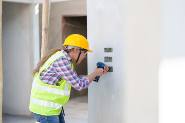 Asian woman drilling screw into apartment wall with cordless drill. Woman wear safety glasses and hand holding drilling tool for apartment renovation. Woman working home improvement. Break the bias.