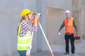 Construction Worker Using Theodolite Surveying Optical Instrument for Measuring Angles in Horizontal and Vertical Planes on Construction Site. Engineer and Architect Using blueprint Next to Surveyor.