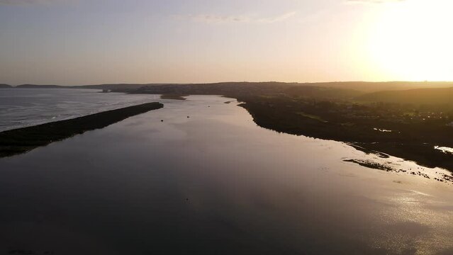 Sunset aerial arc over Keurbooms river estuary shows sandbank separating two water bodies, Robberg Nature Reserve peninsula on horizon