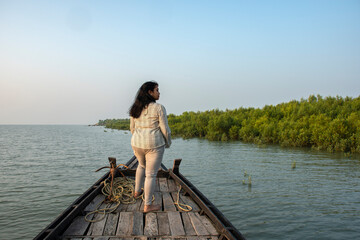 An young solo traveler standing on the adge of a country boat looking at the mangrove forest of Sundarban Tiger Reserve.