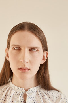 Handsome young male with long hair wearing spotted blouse and rolling up eyes while standing against gray background