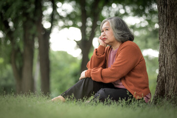 Obraz premium An elderly woman with gray hair sat alone sadly under a tree in the garden.