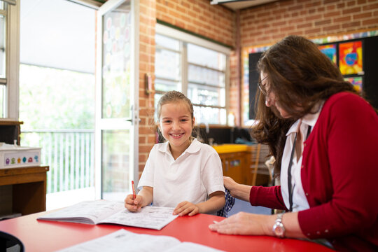 Teacher Helping Young Schoolgirl Smiling at the Camera