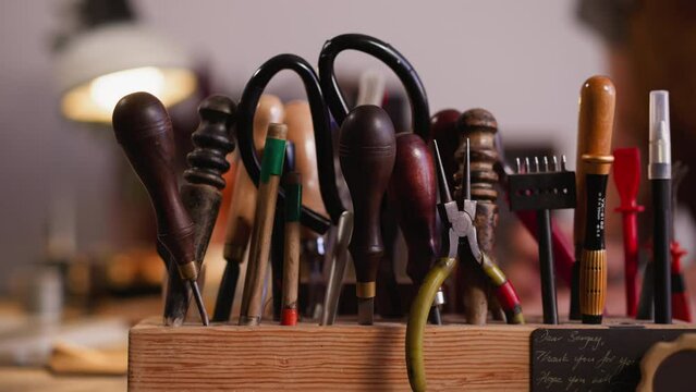 Wooden rack with kit of different leathersmith tools on workbench closeup. Instruments of professional craftsman in workshop. Manual work supplies