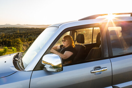 Woman in four wheel drive car driving on country road trip adventure at sunset