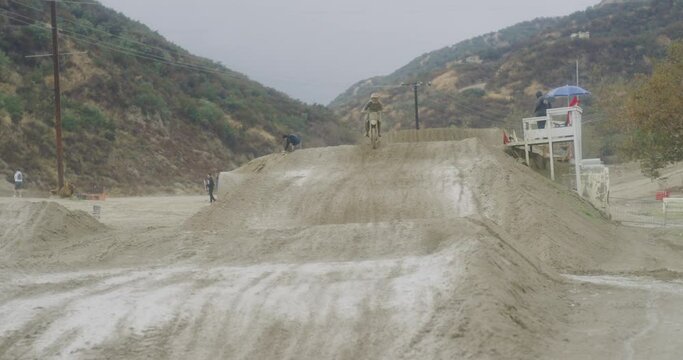 Dirt biker covered in mud jumping on track.
