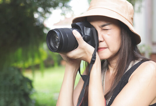 Asian woman wearing hat and sleeveless top  taking photos in the park with dslr camera.