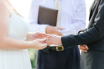 The groom and the bride are wearing rings for the engagement ceremony at the wedding. with the pastor witnessing the closeness of the couple.
