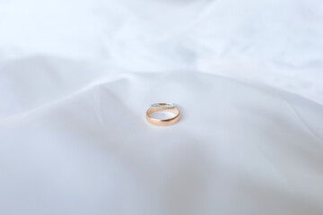 Two engagement rings with a diamond ring and a gold ring stacked in the center on a white cloth on the bed. There is empty space around.