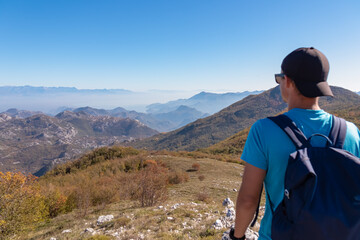 Man with backpack and hat on top of Goli Vrh with scenic view on mountain chains of Dinaric Alps and Lake Skadar National Park, Montenegro, Balkan, Europe. Valley covered by mystical fog. Freedom