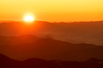 The glowing sun rising over mountains range on a cold winter day, the landscape of mountains on the morning mist. 