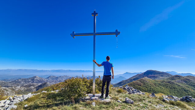Man standing next to the summit cross of mountain Goli Vrh. Panoramic aerial view on dramatic karst mountain chains Dinaric Alps surrounding the Lake Skadar National Park, Montenegro, Balkan, Europ